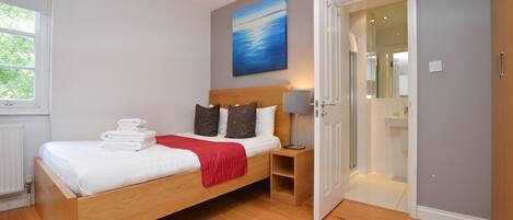Un dormitorio moderno con una cama de madera, un plaid rojo y una mesita de noche con una lámpara.