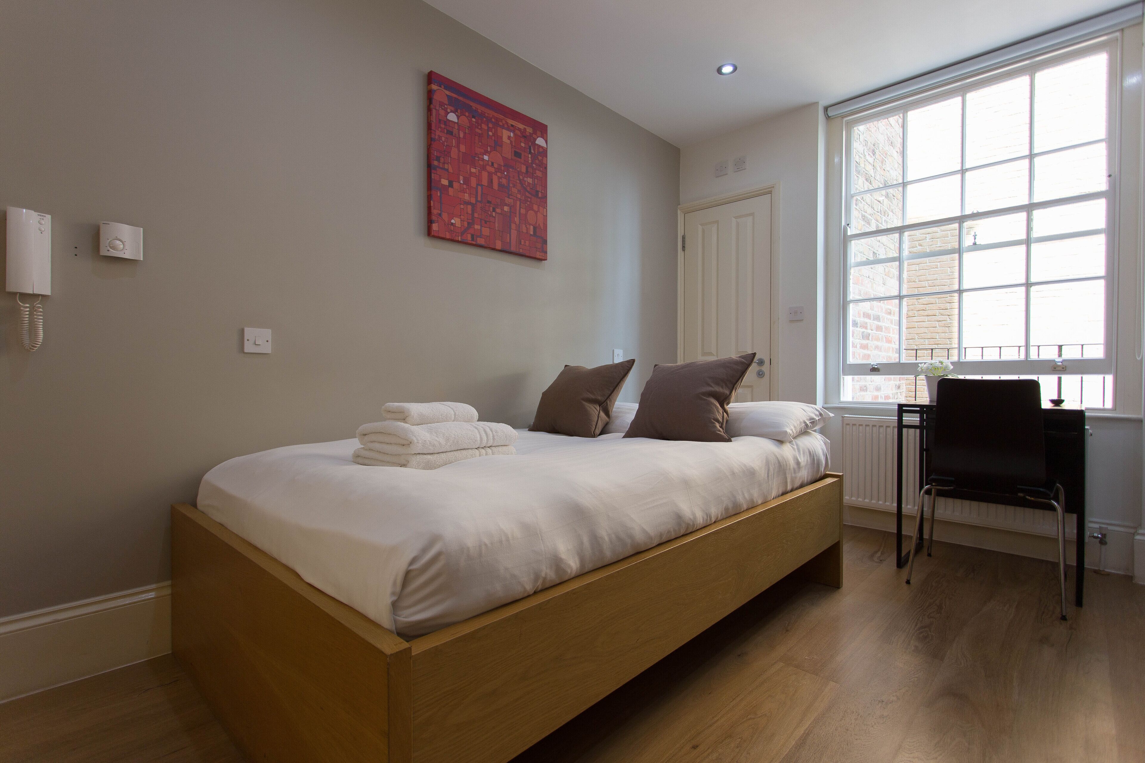 A modern bedroom with a wooden bed, a desk, and a large window.