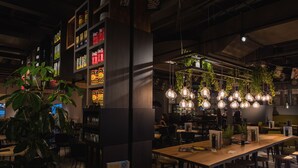 A modern restaurant with a long wooden table, hanging light fixtures, and a variety of plants. - Hotel Meerkerk (Meerkerk)