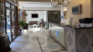 A hotel lobby with a reception desk, a chandelier, a sofa, and a television. - Grand Anzac Hotel (Çanakkale)