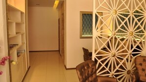 A hallway with a decorative white partition, a brown leather chair, and a shelving unit with books. - Grand Anzac Hotel (Çanakkale)