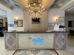 A reception desk with the ANZAC GRAND logo, a chandelier, framed certificates, and a map on the wall. - Grand Anzac Hotel (Çanakkale)
