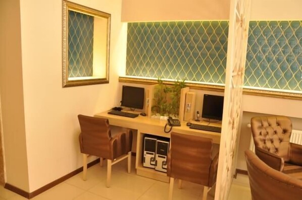 A hotel room with a desk, two monitors, a telephone, and two chairs.