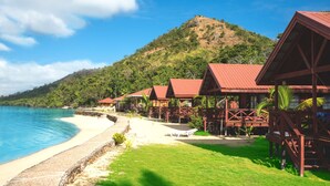 Un resort frente a la playa con cabañas de madera, una playa arenosa y una montaña al fondo.