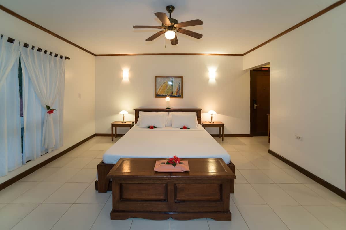 A hotel room with a bed, bedside tables, a ceiling fan, and a painting on the wall.