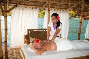 A massage therapy session on a wooden bed with a bamboo structure and white curtains, overlooking a body of water. - El Rio y Mar Resort (Coron)