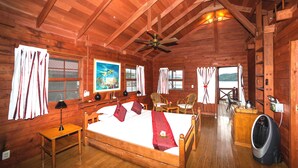 Una habitación de cabaña de madera con una cama, sillas, una mesa y un ventilador.