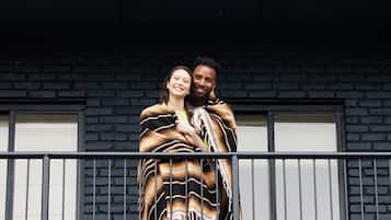 A couple embracing on a balcony with a brick wall and windows in the background.