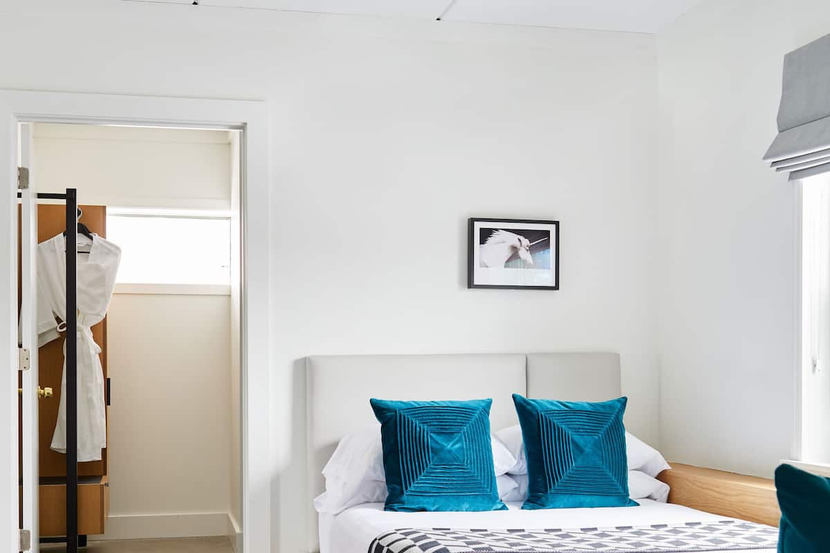 Ein Schlafzimmer mit einem Bett, einem gerahmten Bild an der Wand und einem Kleiderschrank mit Kleidung.