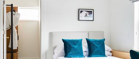 A bedroom with a bed, a framed picture on the wall, and a closet with hanging clothes.