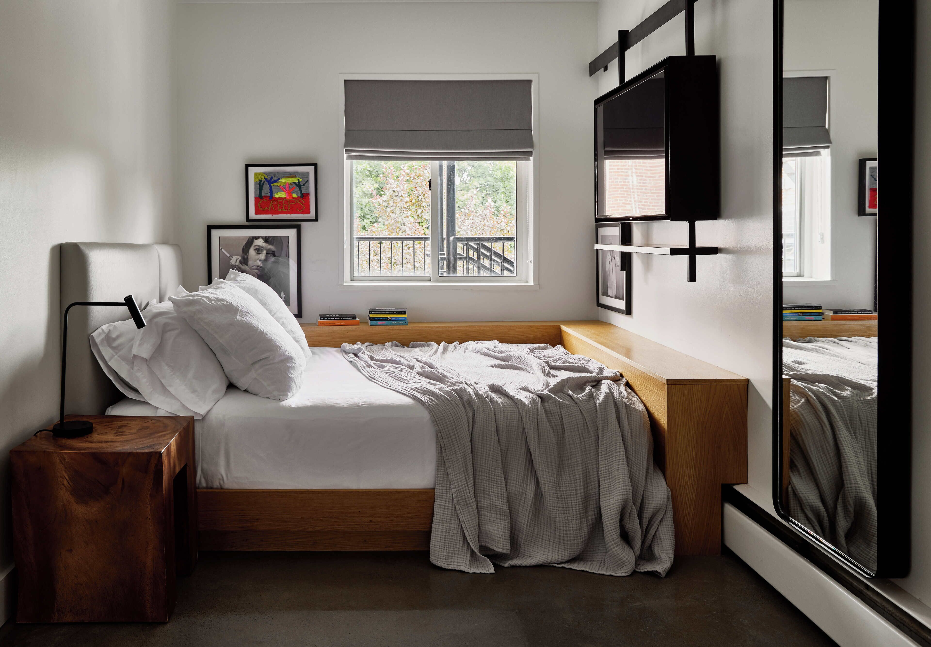 A bedroom with a wooden bed, a bedside table, a window with a view, and a mirror.