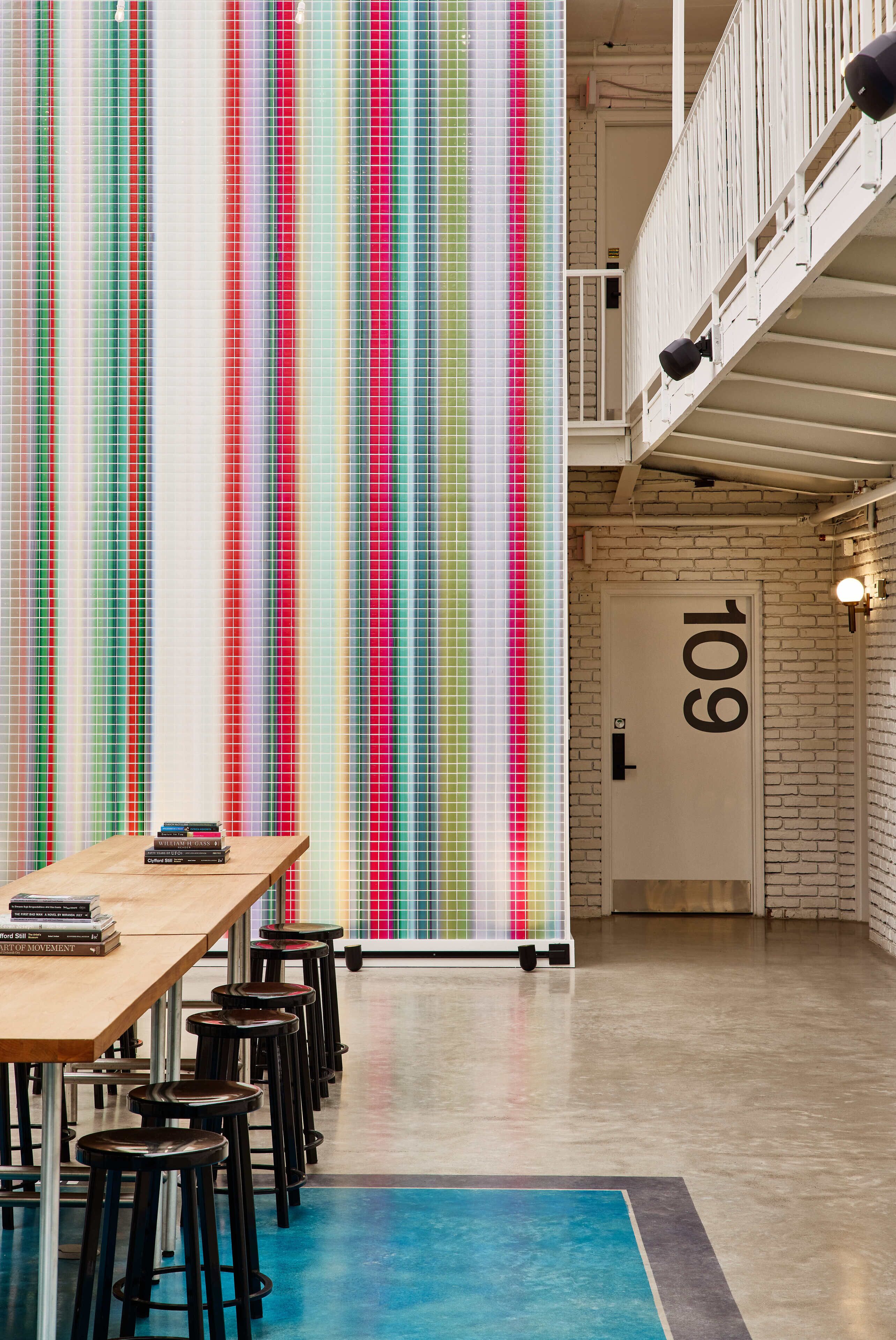 Un interior moderno con una larga mesa y taburetes de bar, una pared colorida a rayas y una puerta blanca con el número 109.