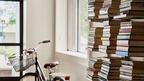 Una habitación con suelo de madera, una bicicleta con canasta y una pared con una gran pila de libros.