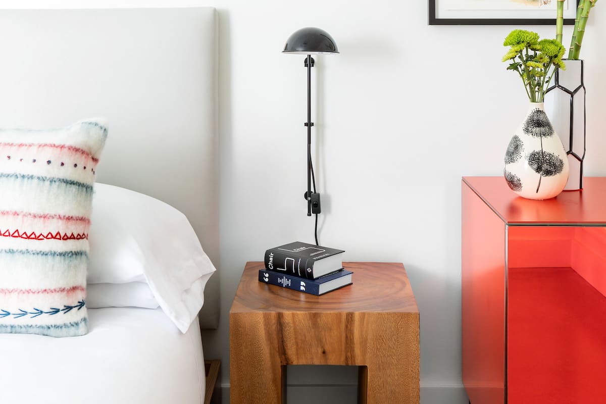 Ein ordentlich eingerichtetes Schlafzimmer mit einem Bett, einem Nachttisch, einer Lampe und einem roten Schrank.