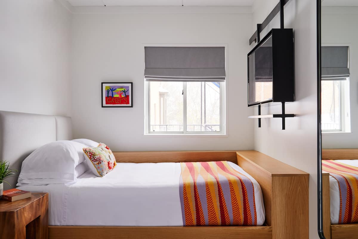 Ein modernes Schlafzimmer mit einem Einzelbett, einem Nachttisch, einem Fenster mit Blick und einem am Wand befestigten Fernseher.