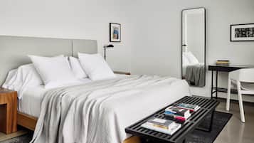 Una habitación de hotel moderna con una cama grande, una mesita de noche, un escritorio con una silla, un espejo y una estantería.