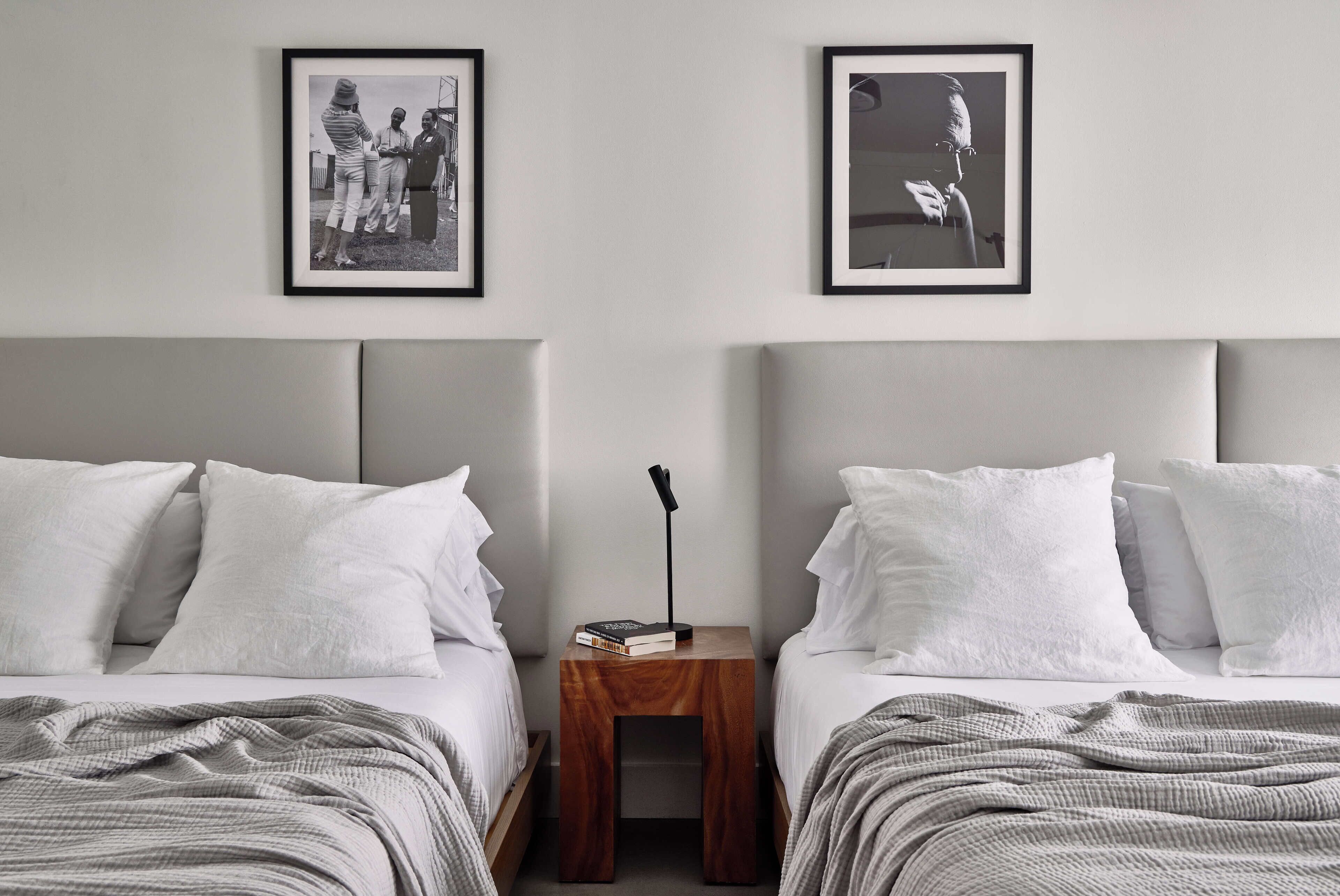 A hotel room with two beds, each with white bedding and pillows. There are two framed black and white photographs on the wall above the beds.
