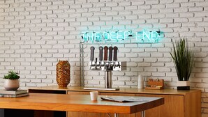 Zona de bar con un letrero de neón que dice “THE DEEP END”, una grifería de cerveza, taburetes y una pared de ladrillo.