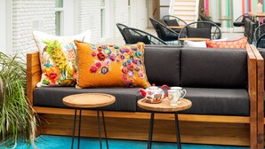 Un rincón acogedor con un sofá, dos mesas redondas de madera y almohadones coloridos.