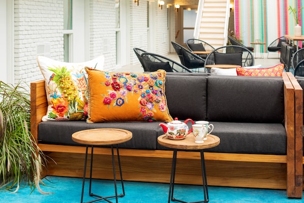 A cozy seating area with a sofa, two round wooden tables, and colorful pillows. - Bluebird Spa City Motor Lodge (Saratoga Springs)