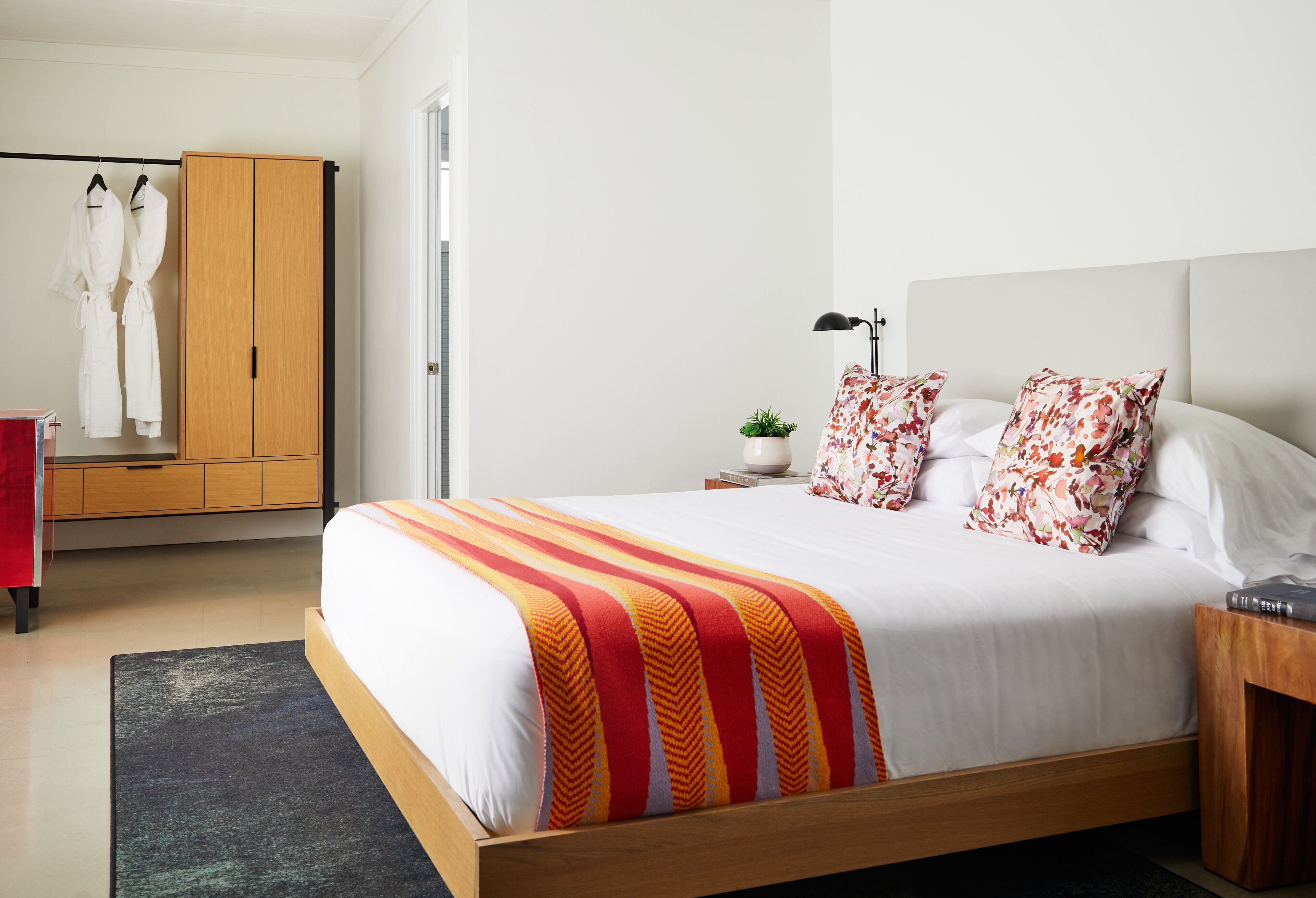 A bedroom with a large bed, a wardrobe, a bedside table with a lamp, and a red chair.
