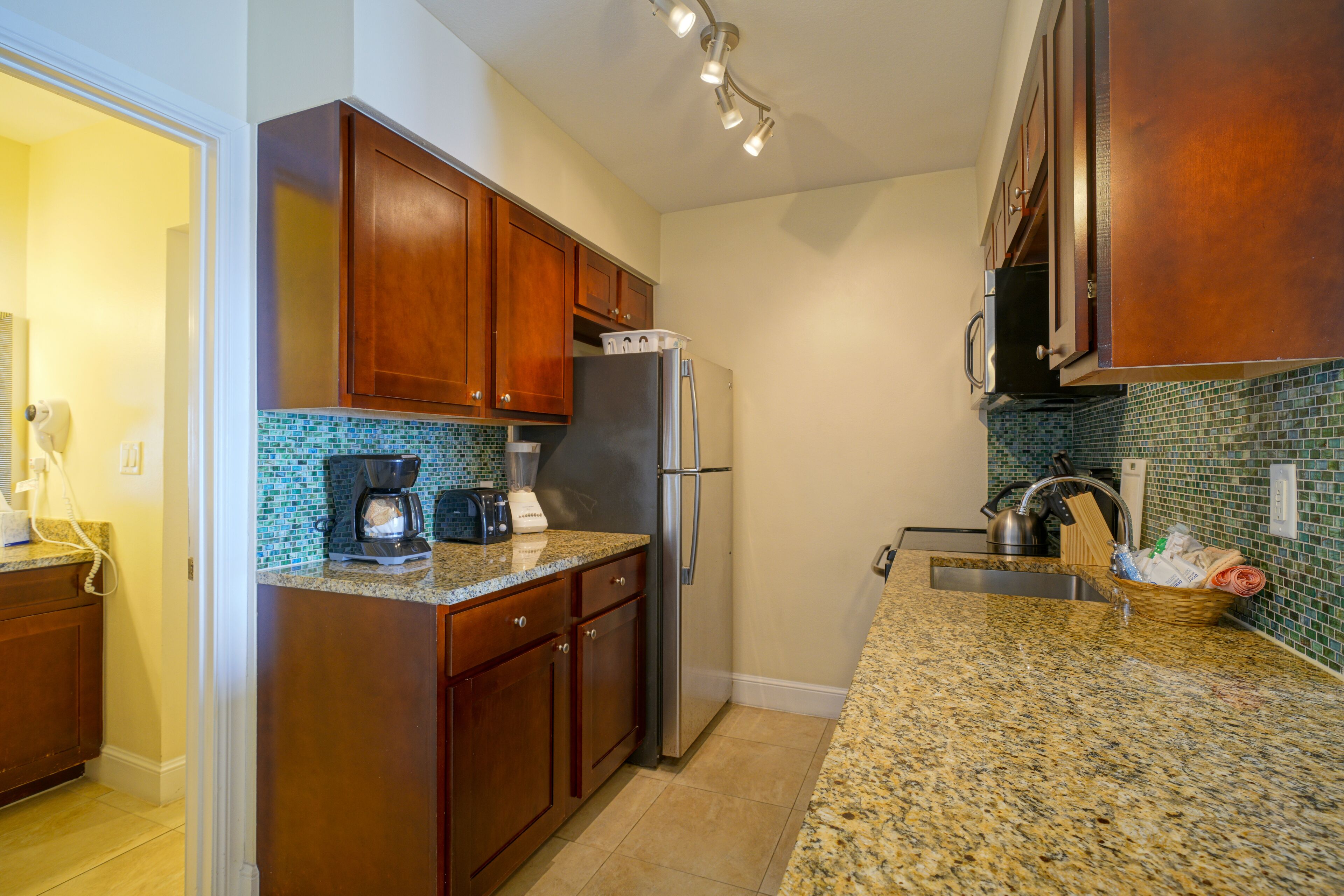 A kitchen with wooden cabinets, a stainless steel refrigerator, a coffee maker, and a sink with a tiled backsplash.