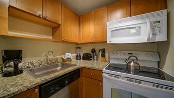 A kitchen with wooden cabinets, a stainless steel sink, a built-in microwave, a stove with a kettle, and a coffee maker.