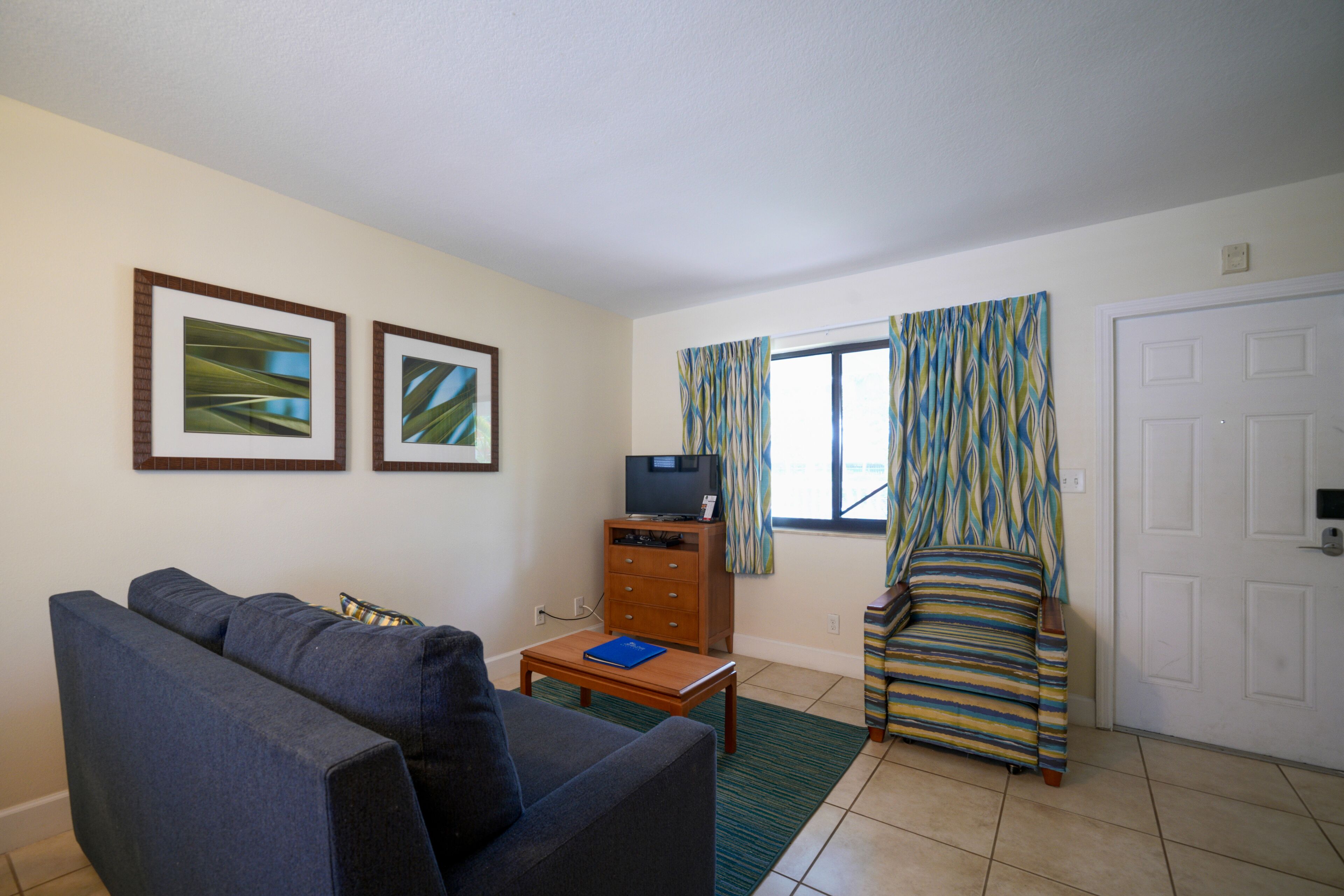 Una sala de estar con un sofá, una mesita, un mueble para la televisión y un ventanal con cortinas.
