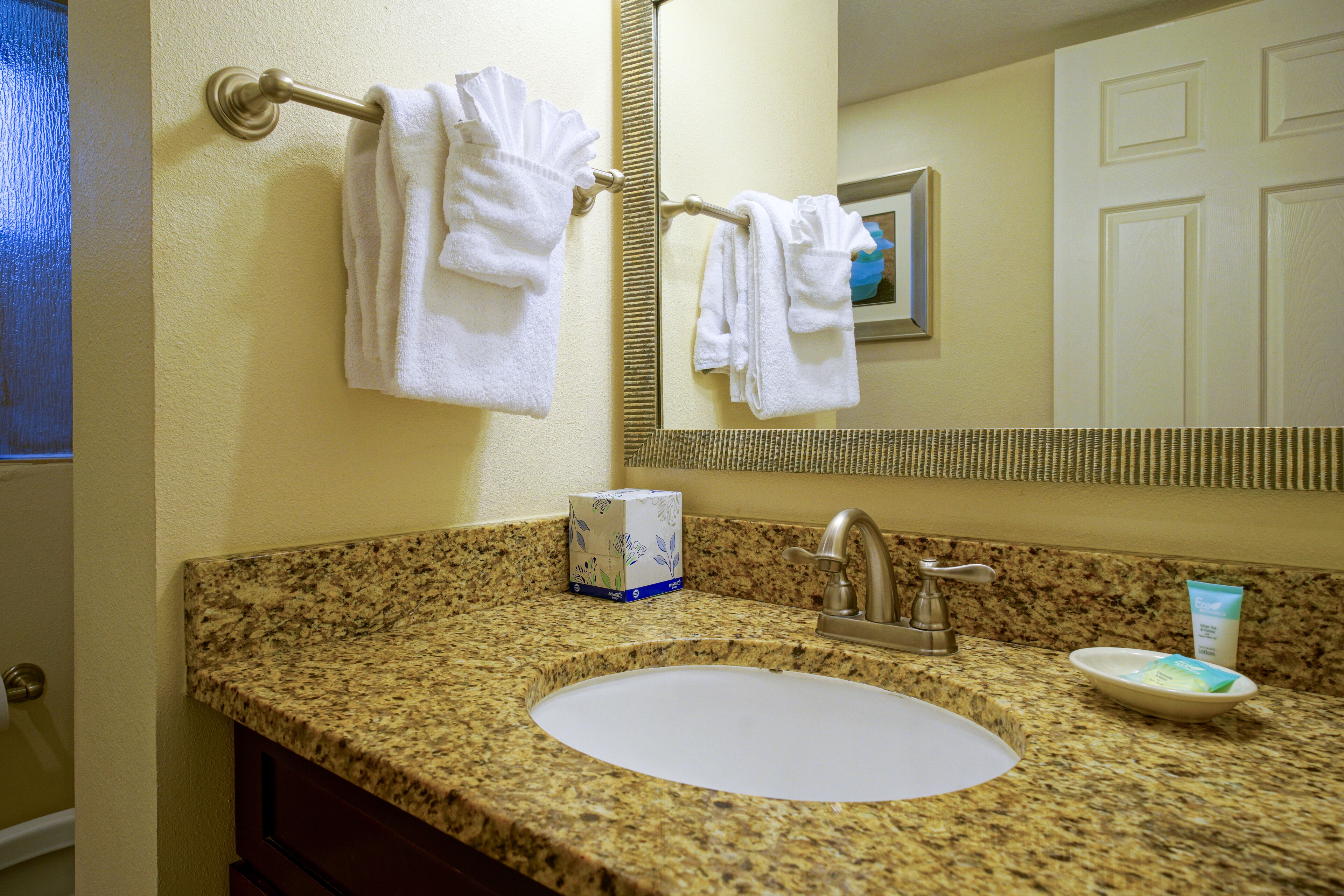 A bathroom with a granite countertop, a white sink, a mirror, and a towel rack with white towels.
