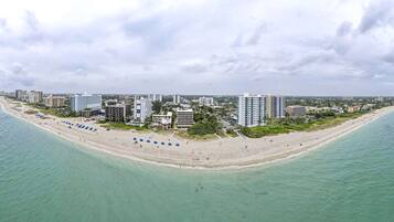 An aerial view of a coastal city with a long sandy beach, numerous high-rise buildings, and a clear view of the ocean.