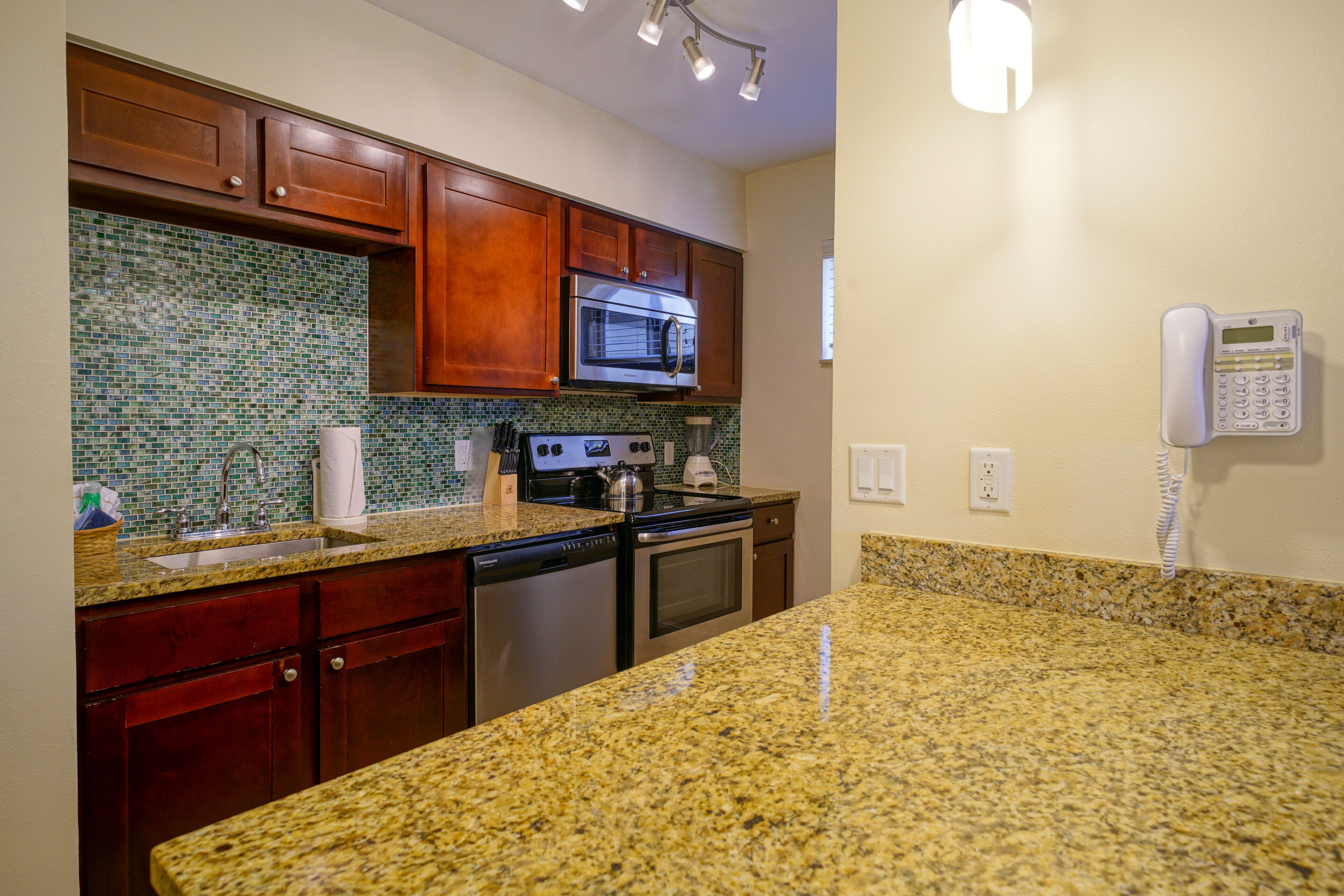 A kitchen with granite countertops, wooden cabinets, a stainless steel microwave, and a built-in oven.
