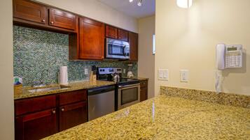 A kitchen with granite countertops, wooden cabinets, a stainless steel microwave, and a built-in oven.
