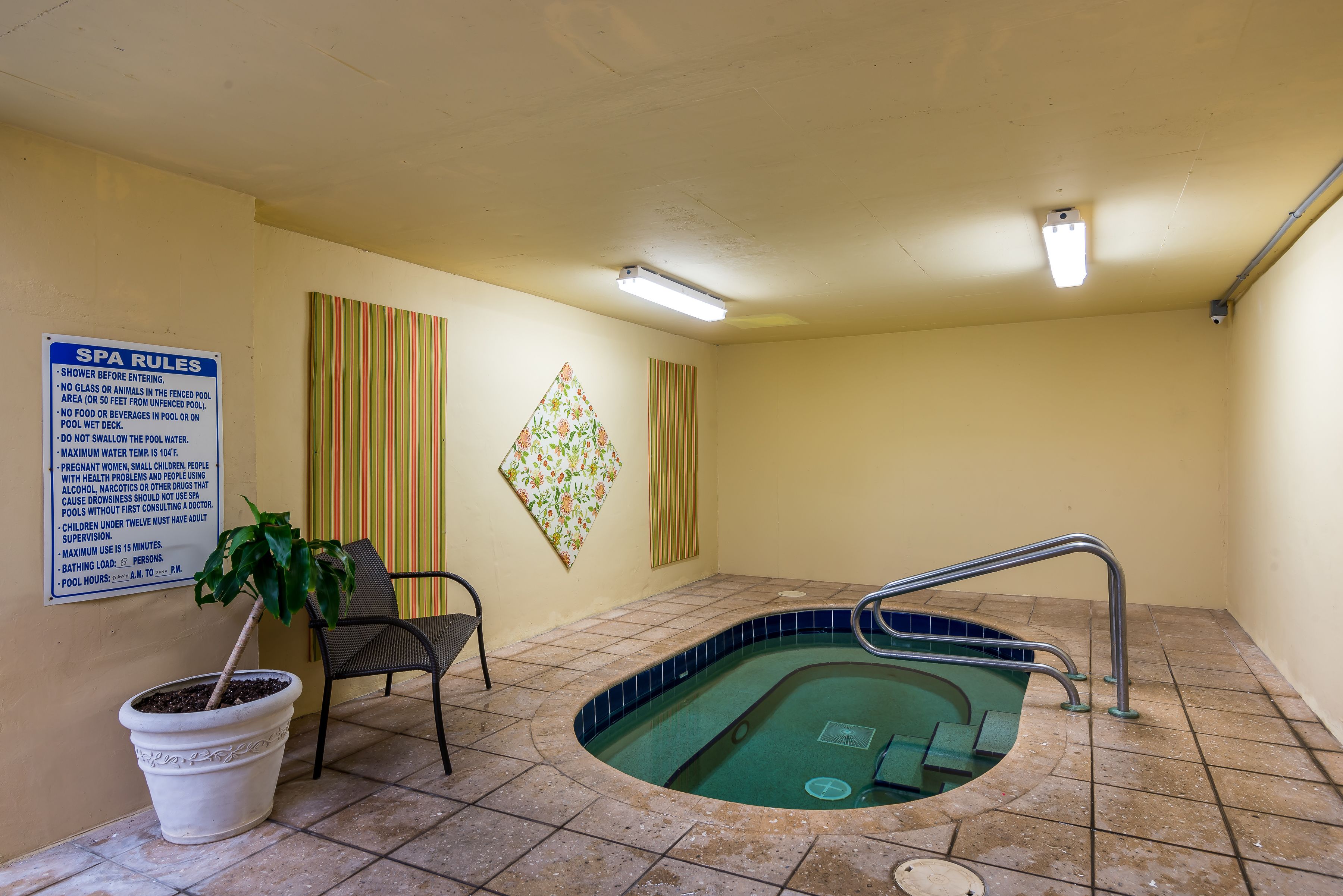 A spa area with a pool, a sign with spa rules, a potted plant, and a chair.