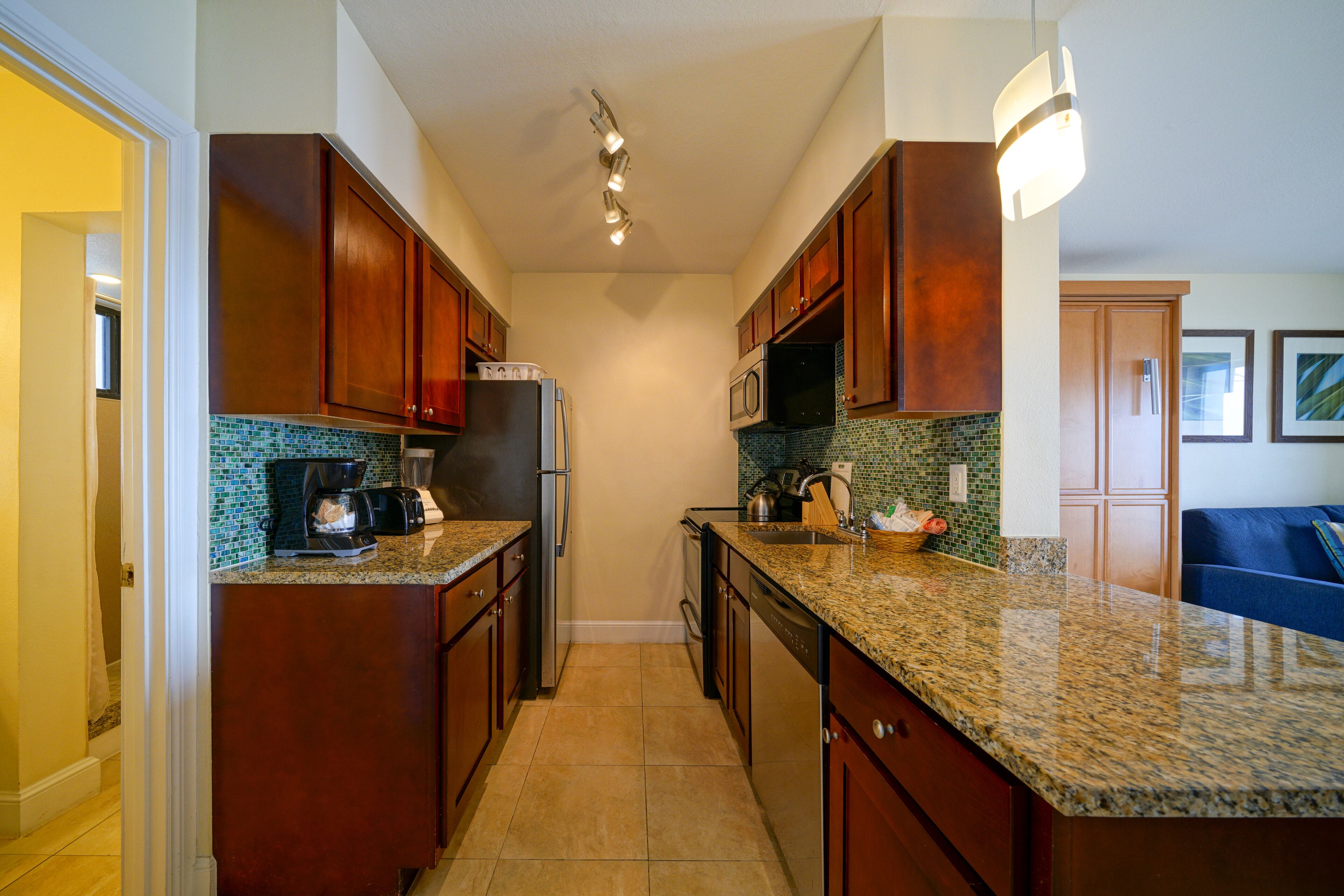 A kitchen with wooden cabinets, granite countertops, a refrigerator, microwave, and a coffee maker.