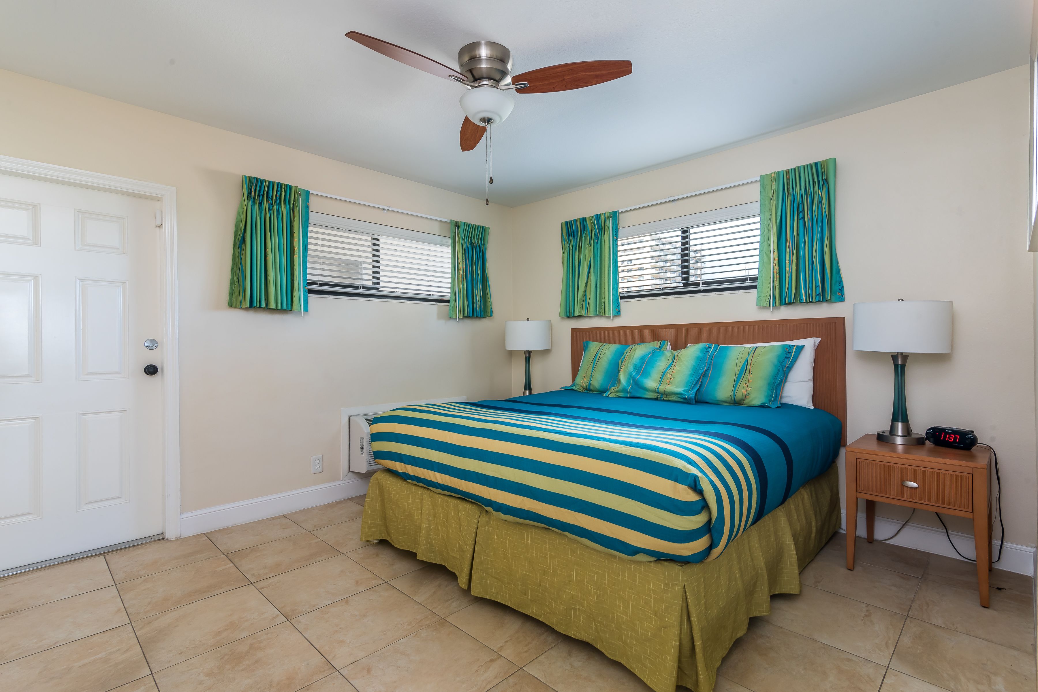 A bedroom with a bed, a ceiling fan, a nightstand, and a window with curtains.