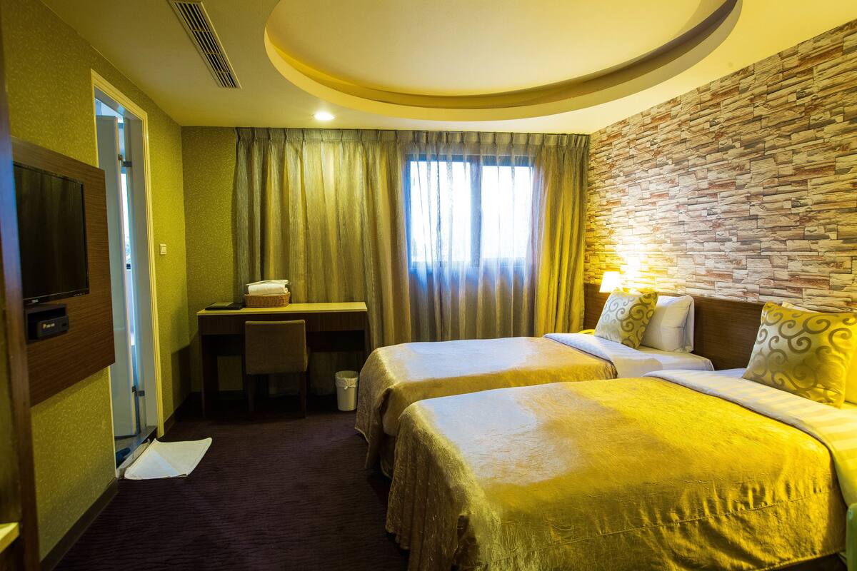 A hotel room with two beds, a desk, a television, and a window with curtains.