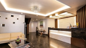 A modern reception area with a sofa, a coffee table with magazines, a chandelier, and a reception desk. - Luckynews Classic Hotel (Taoyuan City)