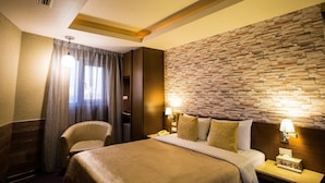 A hotel room with a large bed, a chair, a desk with a telephone, and a stone wall. - Luckynews Classic Hotel (Taoyuan City)