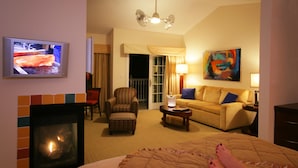A hotel room with a fireplace, a television, a sofa, a chair, and a painting on the wall.