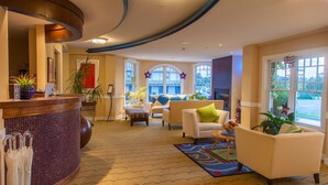 A spacious lobby with a reception desk, comfortable seating, and large windows offering views of the outside.