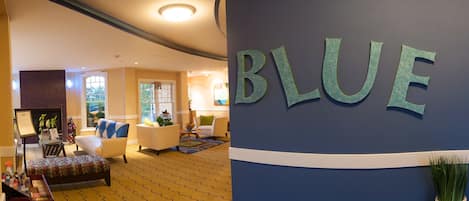 A hotel lobby with a blue wall, a reception desk, and a seating area with chairs and a sofa.