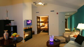 A hotel room with a living area, a TV, a fireplace, and a bed.