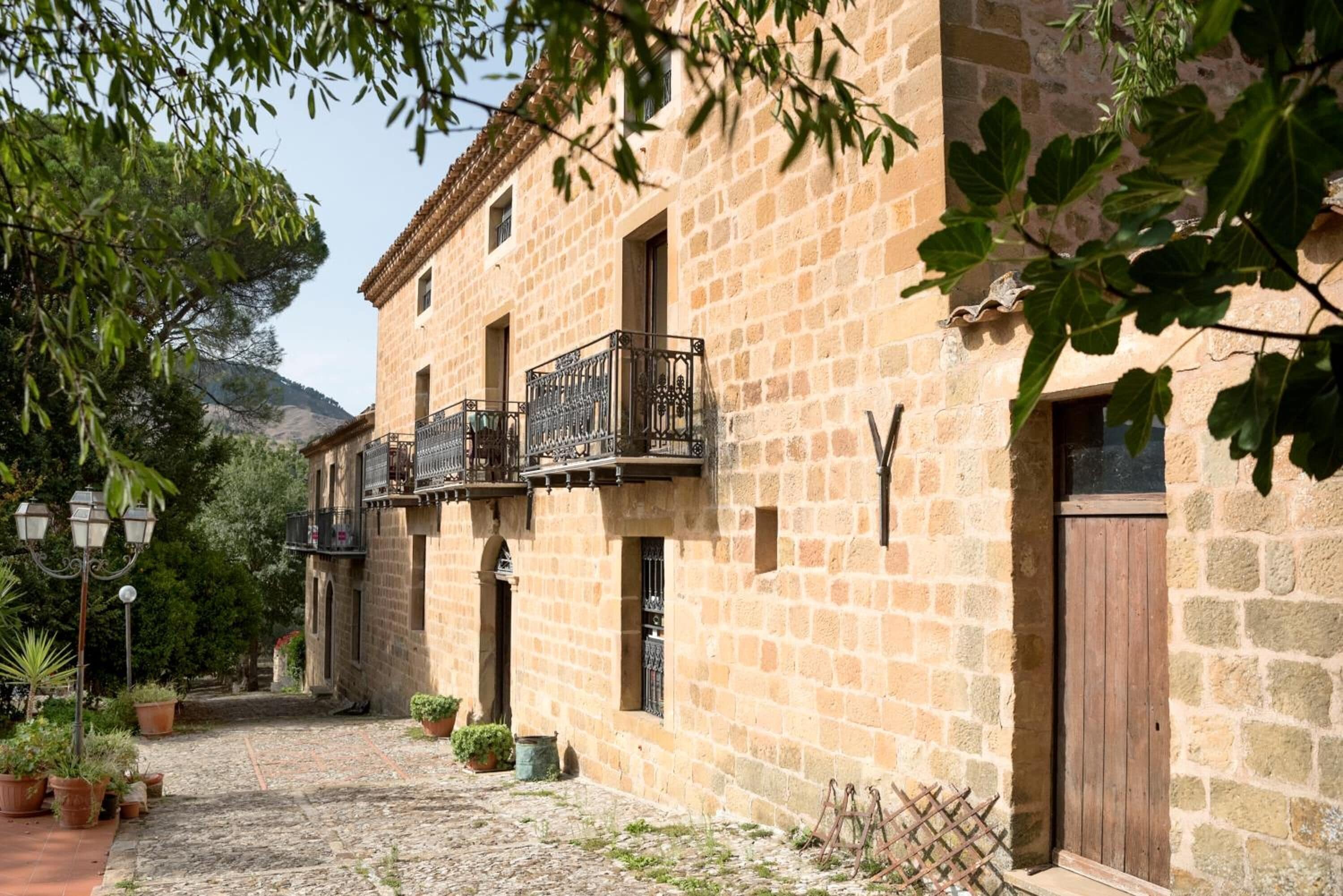 A stone building with a cobblestone courtyard, potted plants, and a wooden door.
