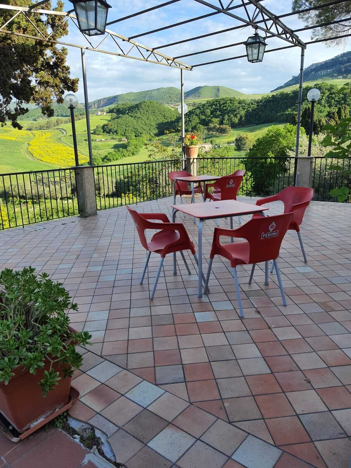 An outdoor patio with a table and chairs, a potted plant, and a view of green hills.
