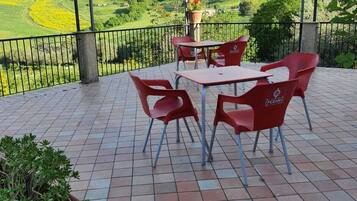 An outdoor patio with a table and chairs, a potted plant, and a view of green hills.