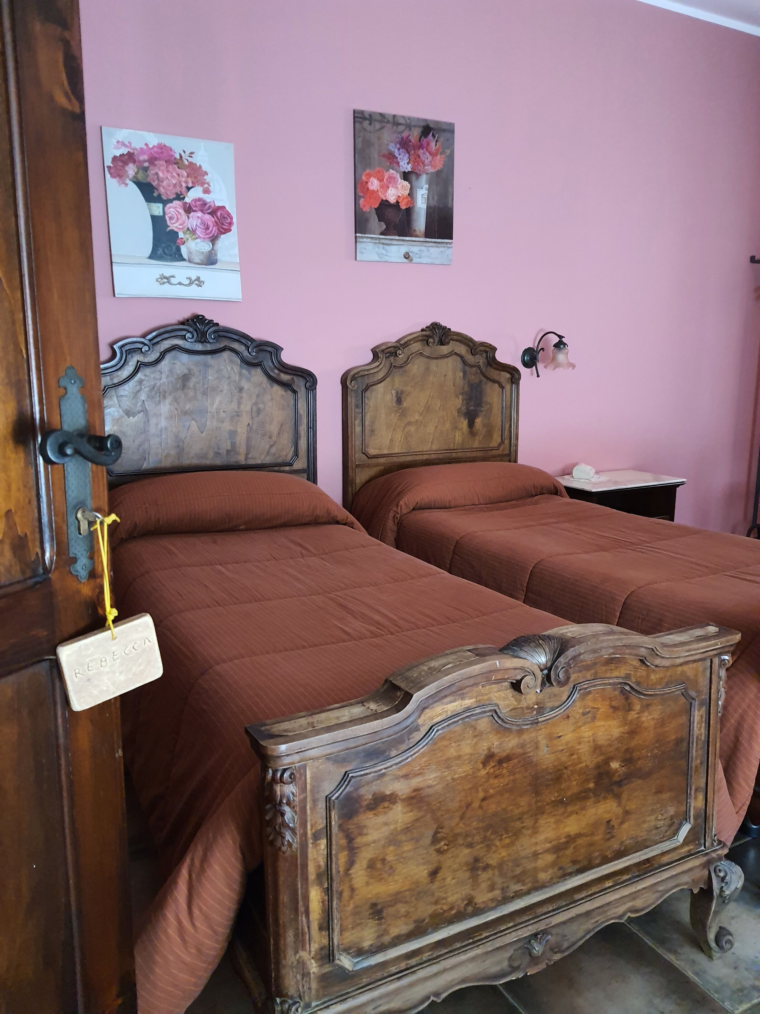 Una stanza con due letti in legno con elaborate testiere, una parete rosa e due dipinti floreali.