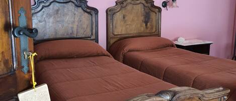 Una stanza con due letti in legno con elaborate testiere, una parete rosa e due dipinti floreali.