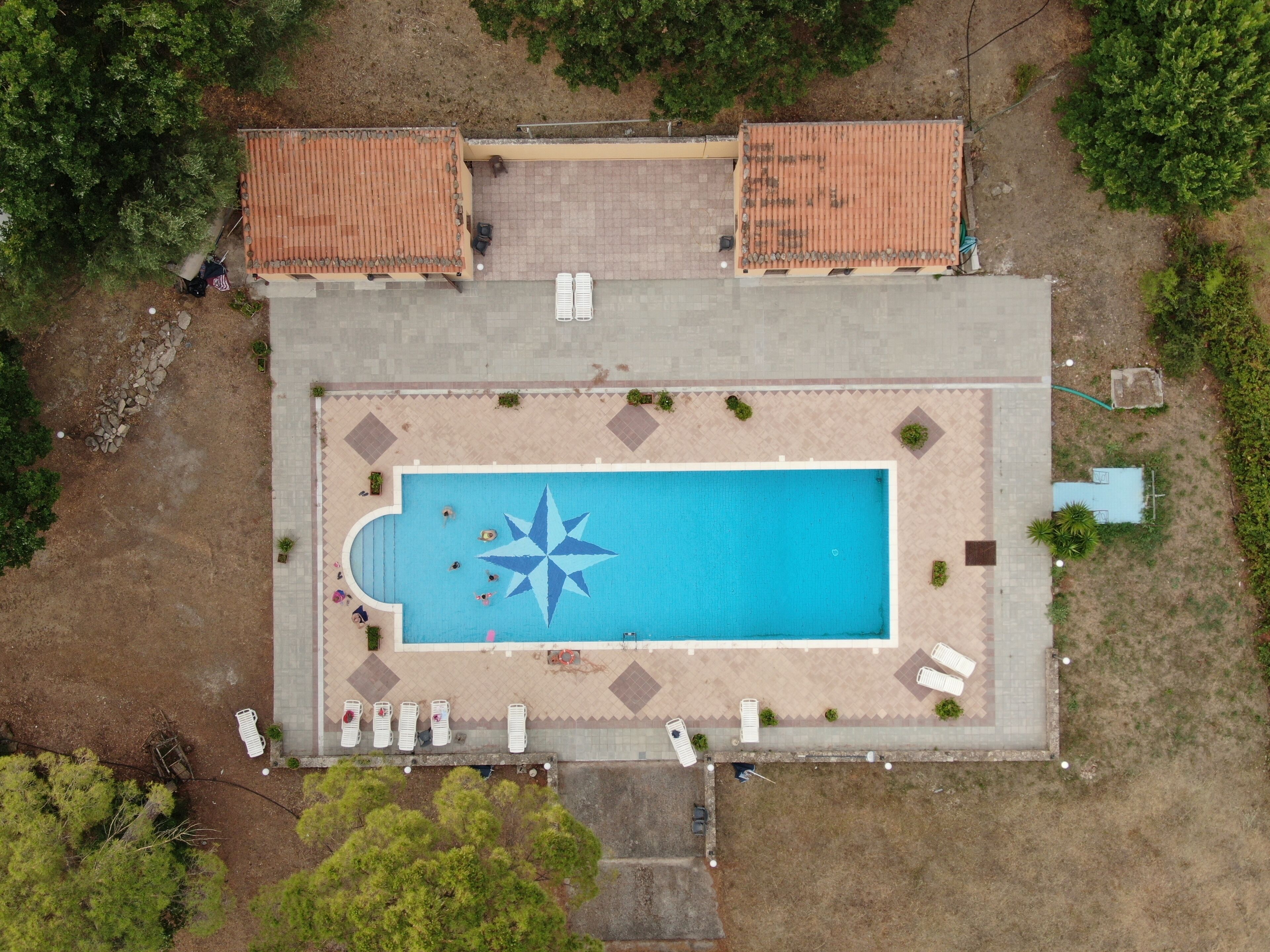 An aerial view of a rectangular swimming pool with a star-shaped design in the center, surrounded by lounge chairs and a tiled deck area.