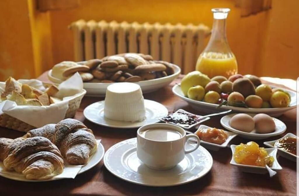 A breakfast table with croissants, a cup of coffee, a bowl of fruits, and a bottle of orange juice.