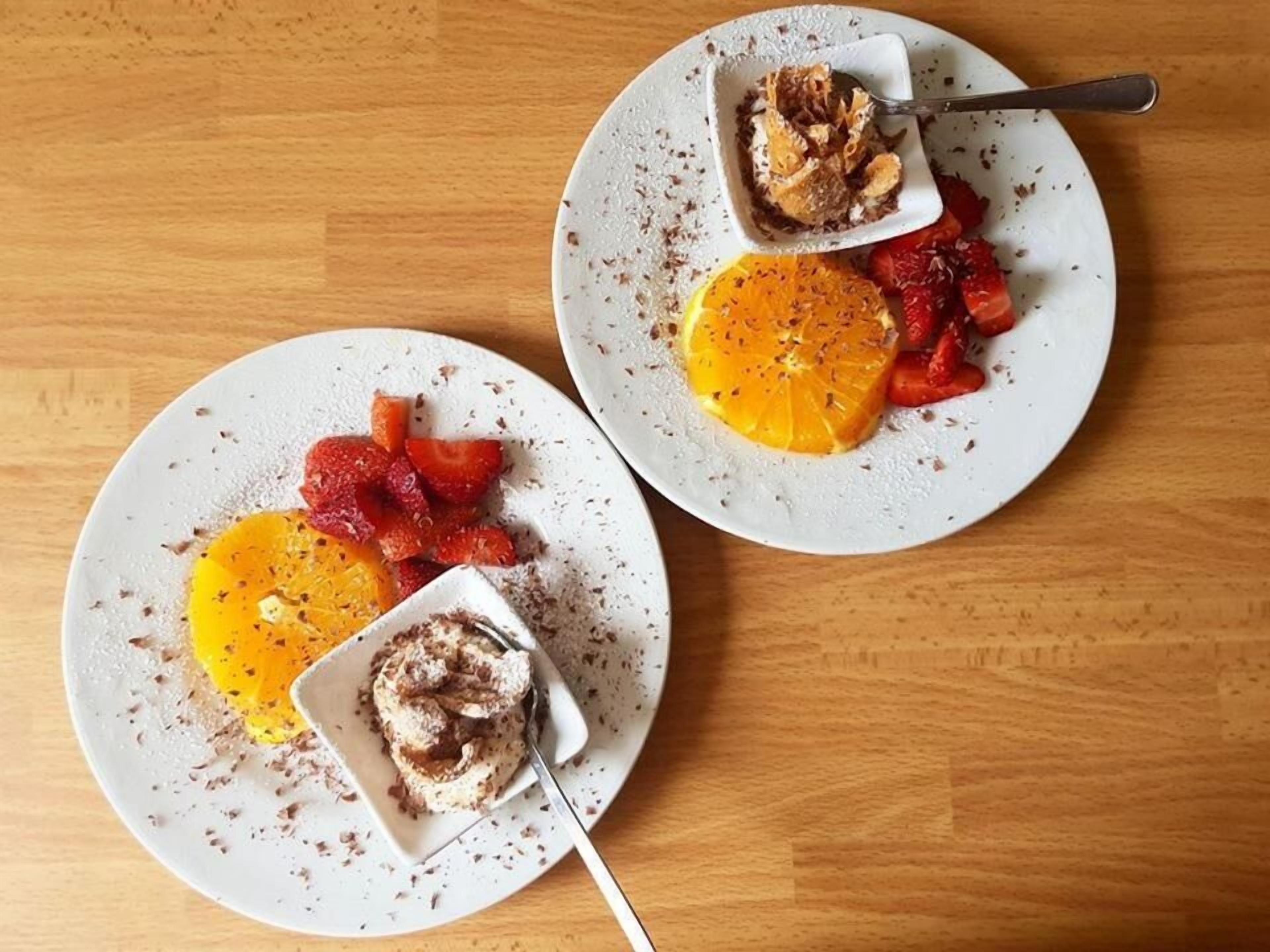 Zwei Teller mit Desserts und Obst auf einem Holztisch.